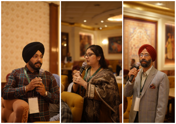 A man holding a clipboard and pen speaks to a seated group in a room with brick walls.